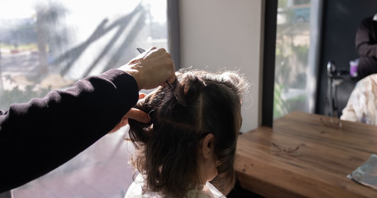 hairdressers near me: hairdresser styling a client's dark hair at a station beside a window